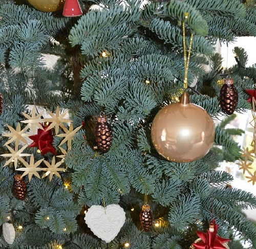 Geschmückter Zweig am Tannenbaum mit Lichtern, Tannenzapen, einem Strohstern und einer goldenen Christbaumkugel